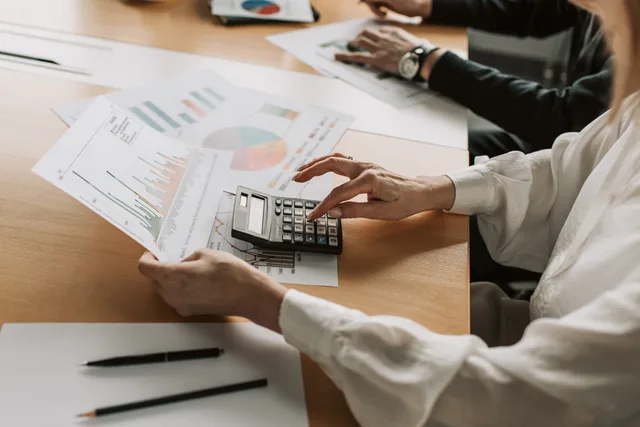 Hands performing financial calculations with charts and a calculator at a meeting table. Five lines to build a SAAS marketing budget from your own revenue