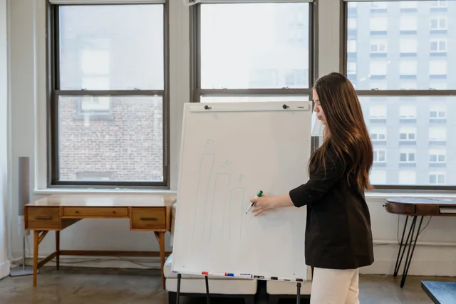 Businesswoman in black blazer presenting on a whiteboard with financial graphs in a modern office. How to define demand signals for SaaS marketing in England