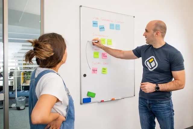Two colleagues brainstorming marketing strategies on a whiteboard. Why a SAAS marketing ninety day plan beats a year of guesswork