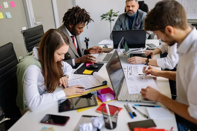 Team of professionals collaborating around a table in a modern office, focusing on projects and discussions. Why a SAAS marketing operating workflow needs owners, not tools
