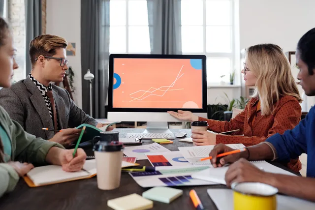 A diverse team discusses data visualization on a computer screen in an office setting. How do I set and audit SAAS marketing service standards?