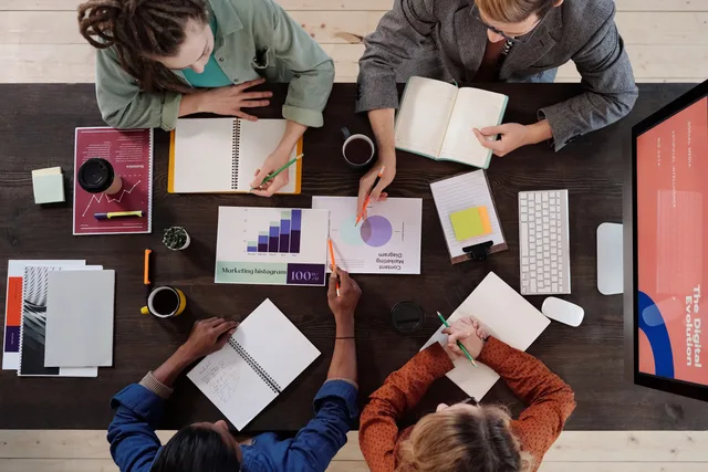 Overhead view of diverse professionals collaborating on a project in a modern office setting. SaaS marketing skills: plan capabilities, not headcount