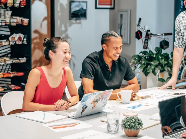 Smiling colleagues brainstorming at work around a table with laptops and documents. Seven steps to build a SAAS marketing strategy your team can run
