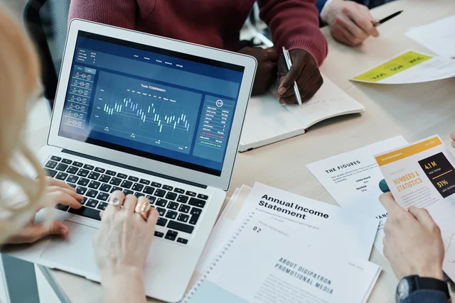 Business professionals analyzing financial data on a laptop during a meeting. Charts and reports visible. SaaS marketing: plan your stack before choosing tools